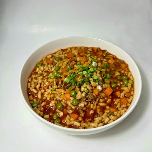 A white bowl filled with Uyghur-style diced noodles, meat, carrots, peas, and green onions in a rich sauce.