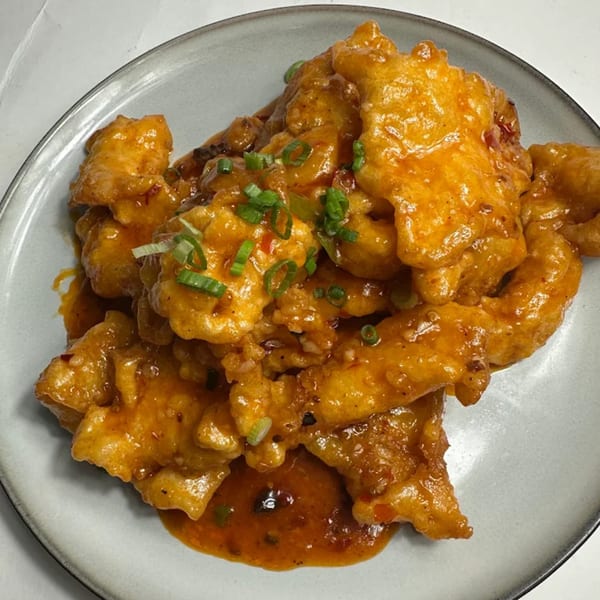 Close-up of golden-fried chicken pieces coated in a glossy orange sauce, garnished with chopped green onions.