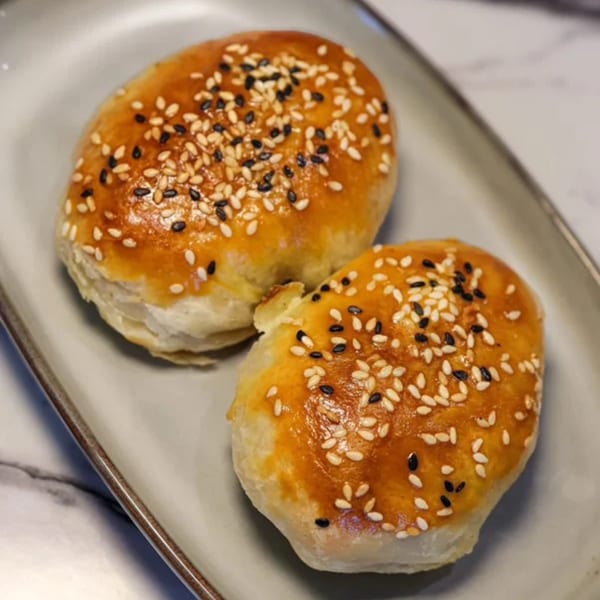 Two golden-brown Uyghur samsa pastries, topped with white and black sesame seeds, on a gray plate.