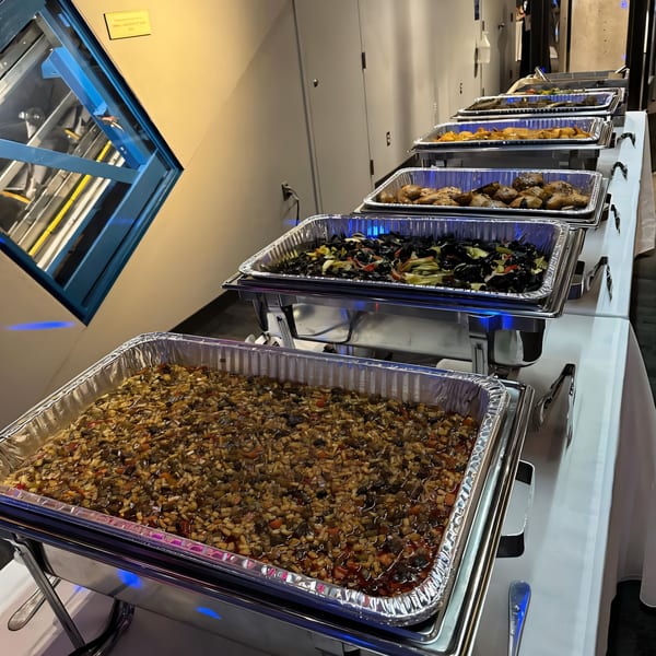 A buffet line of halal Uyghur dishes in chafing dishes, including a stew, mussels, and roasted potatoes.
