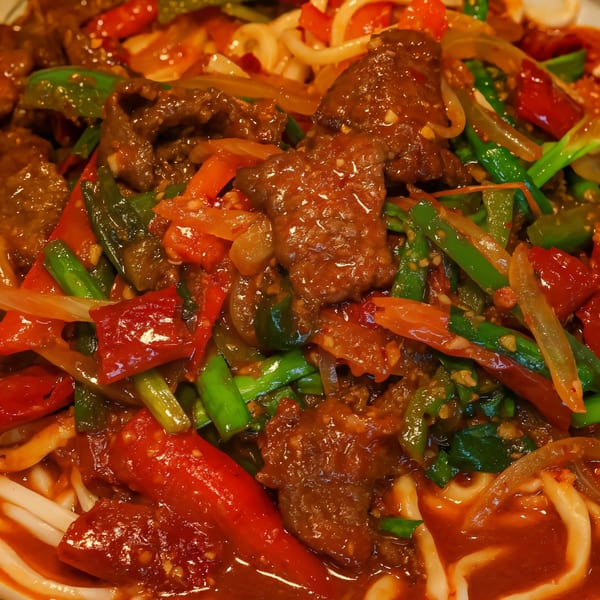 Close-up of Uyghur stir-fried noodles with beef, red and green peppers, and onions in a rich sauce.