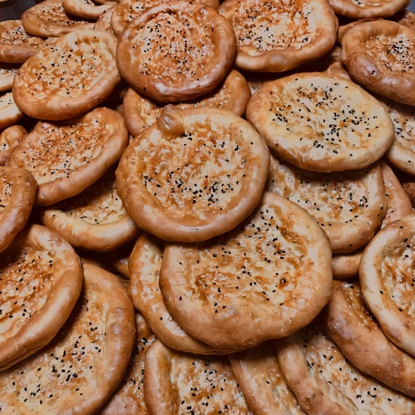 Close-up of many freshly baked Uyghur naan breads, topped with sesame seeds, from Silk Road Uyghur Cuisine.