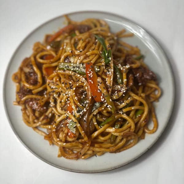 Uyghur stir-fried noodles with vegetables and sesame seeds on a white plate.