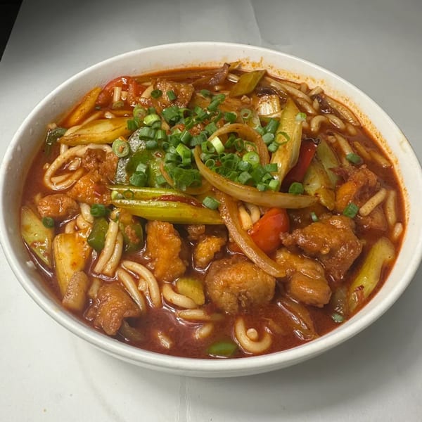 A bowl of Silk Road Uyghur Cuisine's halal noodles with chicken, vegetables, and a savory red sauce.