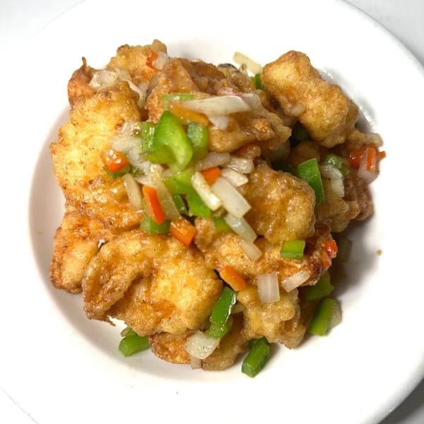 Golden-fried chicken pieces with diced green peppers, onions, and carrots in a white bowl.