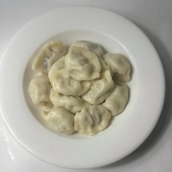 A white plate filled with steamed Uyghur dumplings, known as Manta, on a white background.